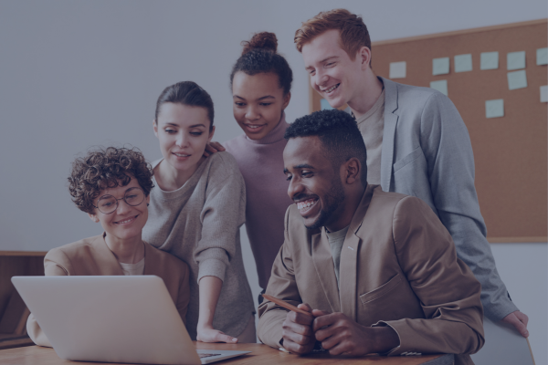A diverse group of young professionals smiling while collaborating on a laptop, capturing teamwork and networking in remote internship environments.
