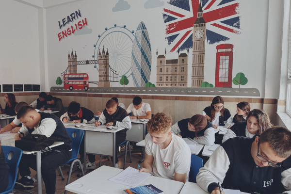 Students learning English in a classroom with London-themed wall art, including Big Ben and the Union Jack flag.