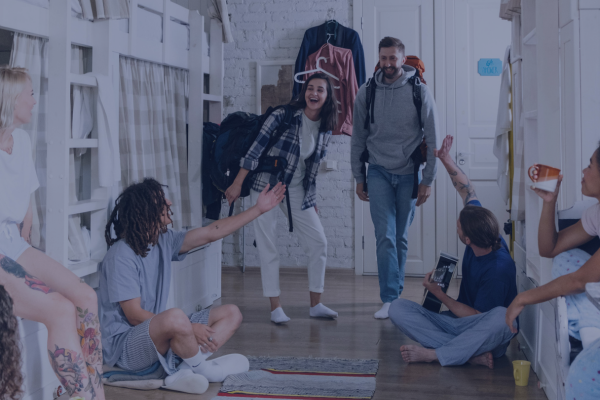 A group of happy travelers socialize in a cozy hostel dormitory, creating a welcoming backpacking atmosphere.