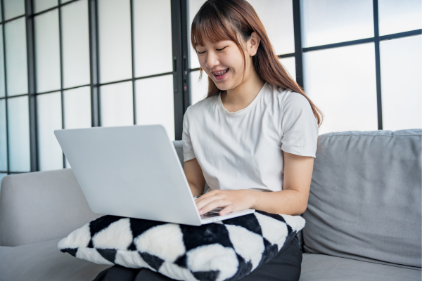 From A1 to C2: Understanding the CEFR English Proficiency Levels 9 Young international student sitting on a couch and studying English online with a laptop on her lap.