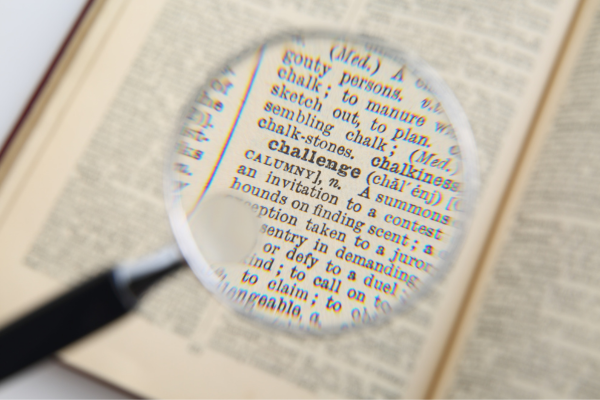 Global Career Skills: 7 Key Skills Employers Expect from International Graduates 9 Magnifying glass focusing on the word challenge in an open dictionary, highlighting detail and meaning.