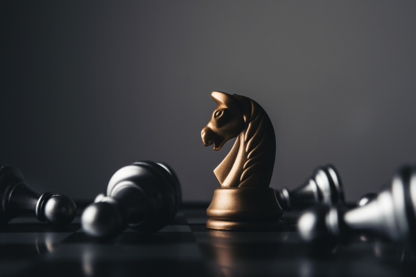 Golden knight chess piece stands amidst fallen pieces on a board, representing strategy and victory.