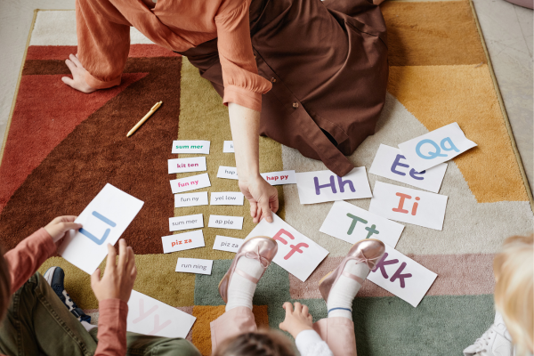 10 Essential Tips for New ESL Teachers: How to Teach English Like a Pro 11 Children learning letters and words with a teacher on a colorful rug. Engaging educational activity with flashcards.
