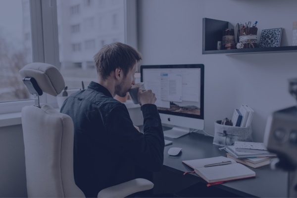 A man drinks from a mug while looking at a computer screen in a home office.