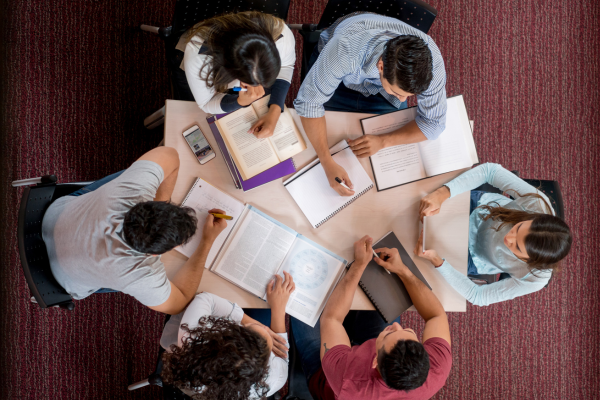 TOEFL vs. IELTS: Which English Proficiency Test Should You Take? 10 Group of students studying together at a round table with books and notebooks, viewed from above.