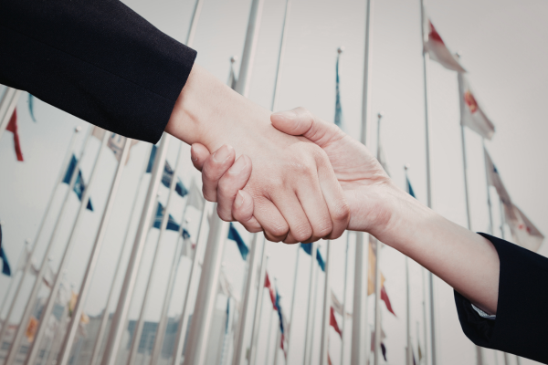 Diplomacy in the 21st Century: New Skills for a Globalized World 6 Handshake between two business people with international flags in the background, symbolizing global partnership.