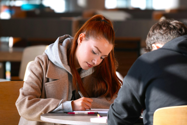 Diplomacy in the 21st Century: New Skills for a Globalized World 7 Student focused on studying in a library, writing notes on paper at a round table.