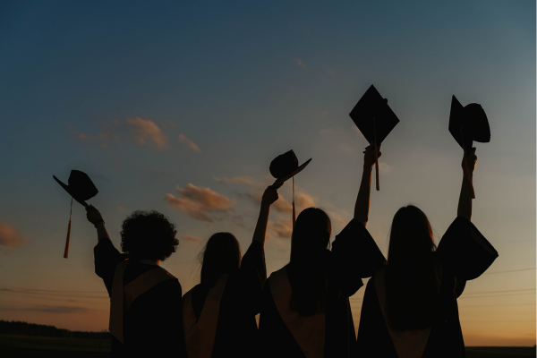 Silhouettes of graduates raising caps against a sunset sky, celebrating academic achievement.