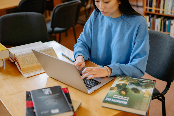 Innovative Study Habits for the Digital Age: Leveraging AI Tools for Students 6 Student studying in a library using a laptop, surrounded by books on a wooden table.