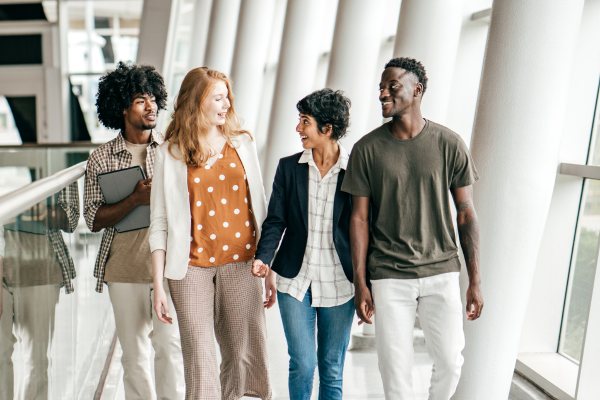 The 2026 U.S. Tuition Fee Report: Trends in Public vs. Private University Costs 5 Group of four diverse young adults walking and talking in a bright hallway, exuding teamwork and inclusivity.