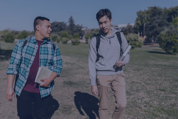 Two students walking on campus with books, talking and wearing casual outfits representing commuter student culture.