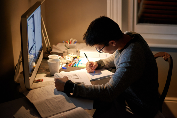 Balancing Work and Study: A Commuter Student’s Guide 10 Person studying at a desk with computer and papers, focused on writing under a lamp's warm light.