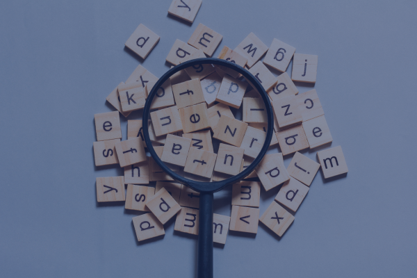 A magnifying glass over wooden letter tiles representing search and keywords on a neutral background.