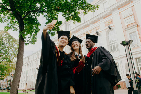 Is Your Degree Worth the Cost? Understanding the ROI of Education in the US 7 Graduates in caps and gowns taking a selfie at a university campus, celebrating their graduation day.