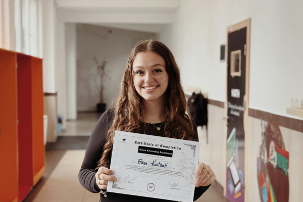 Is Your Degree Worth the Cost? Understanding the ROI of Education in the US 11 Smiling woman holding a certificate of completion in a hallway.