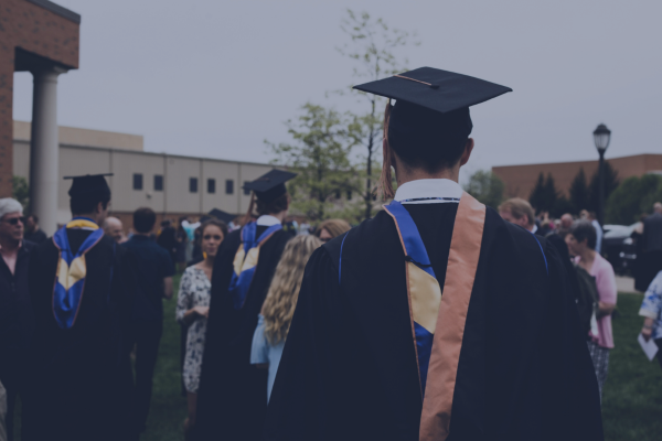 Graduates in caps and gowns gather outdoors, celebrating commencement with family and friends.