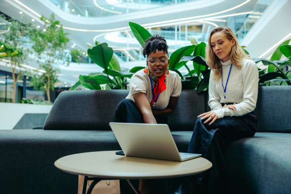 How Career-Focused Universities Help Reduce Student Debt and Improve Career Outcomes 9 Two women discussing work on a laptop in a modern office with greenery and open space.