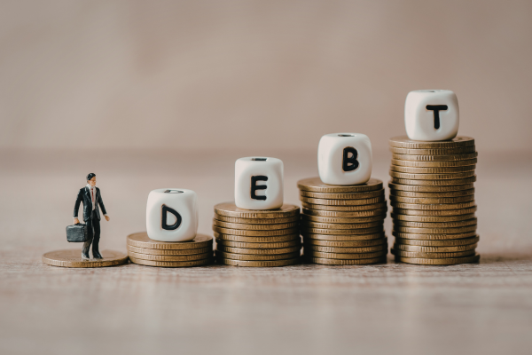 How Career-Focused Universities Help Reduce Student Debt and Improve Career Outcomes 7 Miniature businessman next to stacks of coins with dice spelling DEBT on top.