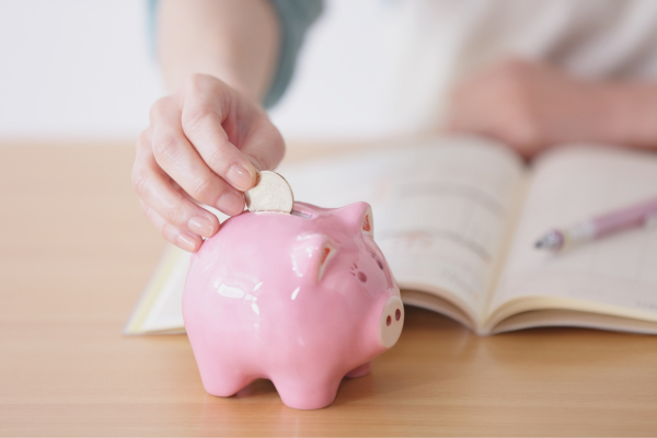Financial Literacy: Managing Multi-Currencies and Budgeting Tips for International Students 7 Hand placing a coin in pink piggy bank with an open notebook in the background.