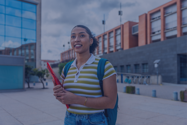 Young woman with a backpack and notebook standing outside modern university building, smiling confidently.