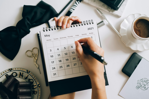 Side Hustles for College Students: Balancing Freelancing with Full-Time Studies 9 Person writing in a May 2021 calendar on a desk with coffee, stationery, and accessories.