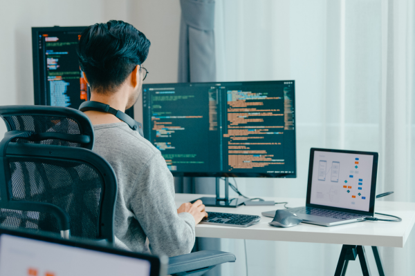 Side Hustles for College Students: Balancing Freelancing with Full-Time Studies 12 Software developer coding on multiple screens at a modern desk setup.