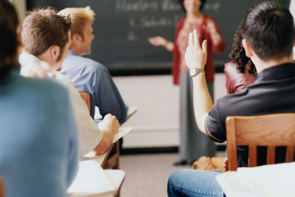 Side Hustles for College Students: Balancing Freelancing with Full-Time Studies 13 Students in a classroom raising hands during a lecture, engaging with a teacher in front of a blackboard.