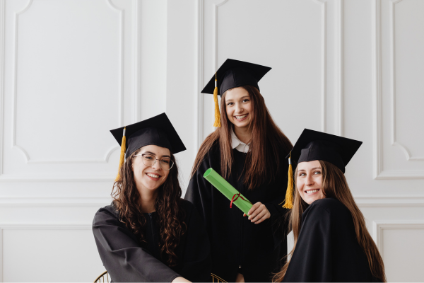 Why Donate to STEM Education? The Ripple Effect of Giving 13 Three graduates in caps and gowns smiling, holding a diploma, celebrating their achievement in a bright room.