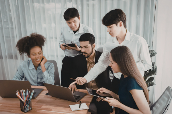 Why Diversity in Business Drives Better Startup Outcomes 10 Team collaborating in office, using laptops and tablets around a table, discussing work strategy and projects.