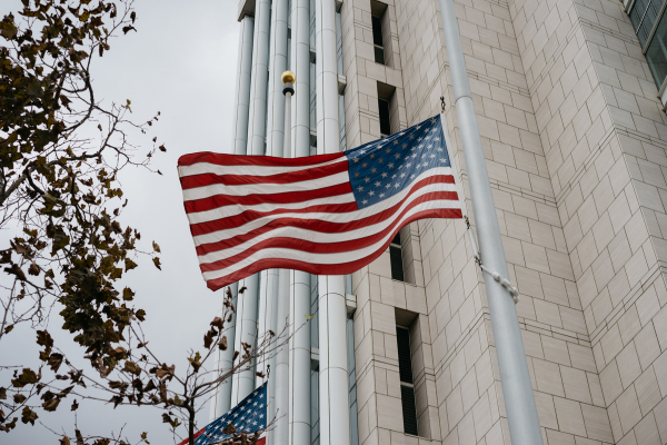 The New F-1 Visa Rules 2026: Simplified for International Students 5 American flag waving outside a tall building on a cloudy day, with autumn leaves in the foreground.