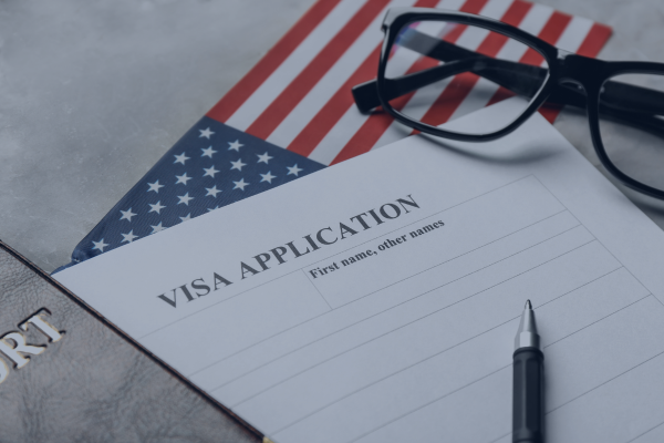 Visa application form with pen on USA flag background, next to glasses and a passport.