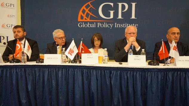 Panel discussion at Global Policy Institute featuring several speakers and flags on a blue backdrop.