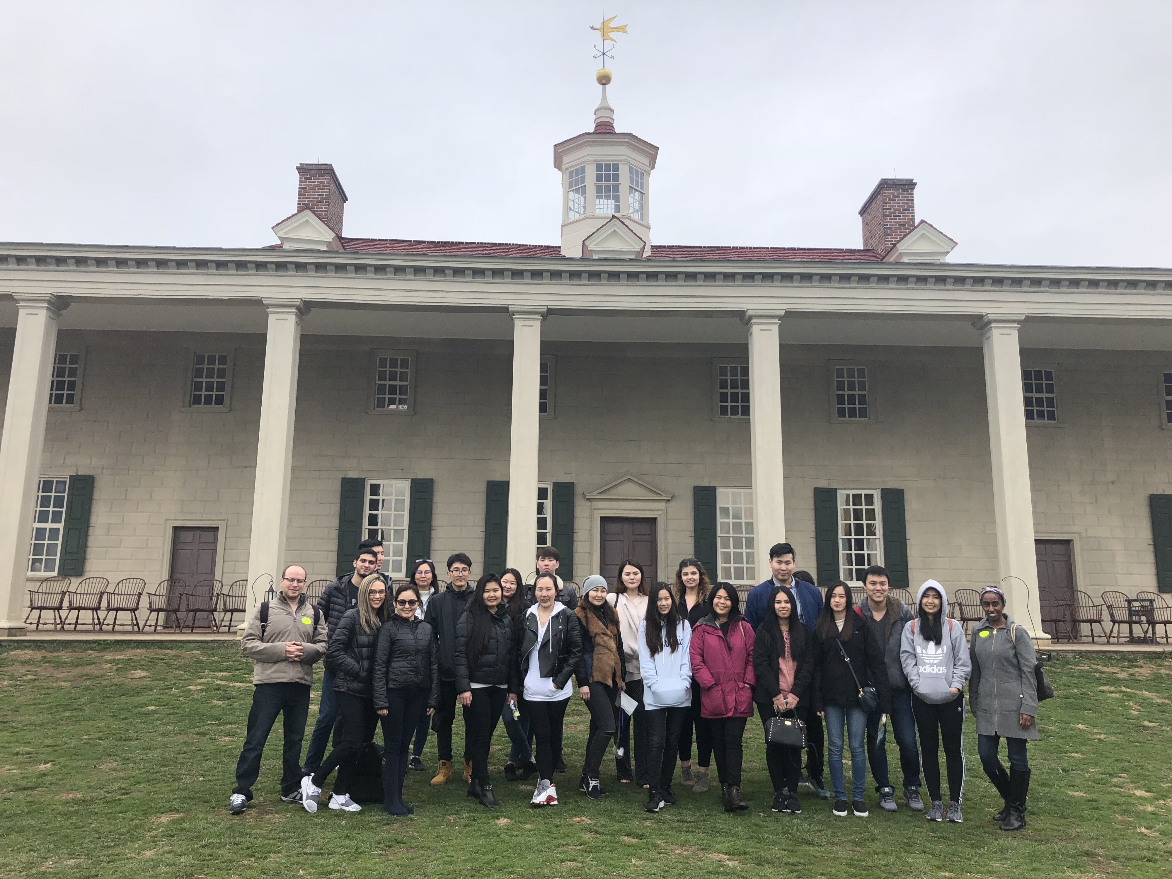 Group of people posing in front of a large historic building with columns on a cloudy day.