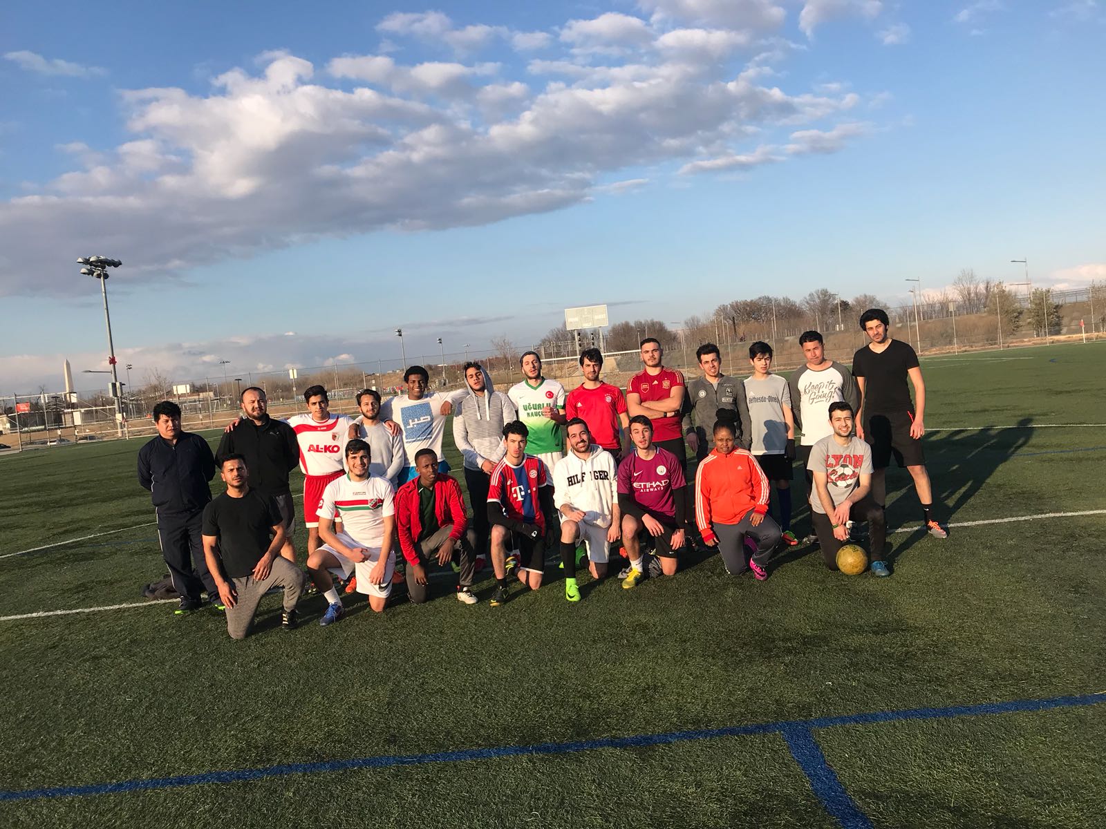 Group of people posing on a sunny day on a soccer field, with a ball on the grass.