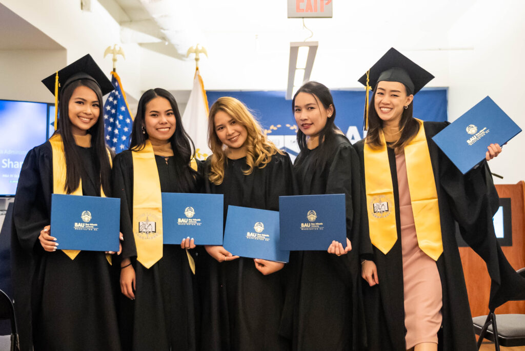 Graduates in caps and gowns celebrate with diplomas at a graduation ceremony with blue and gold accents.