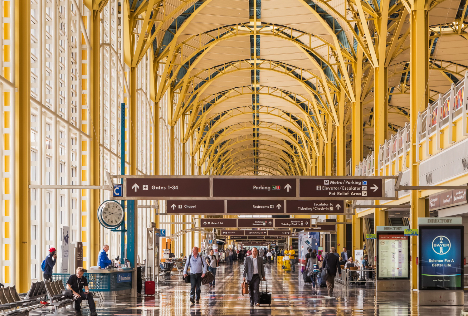 Busy airport terminal with travelers heading to Gates 1-34 beneath an arched ceiling, featuring directory signs.