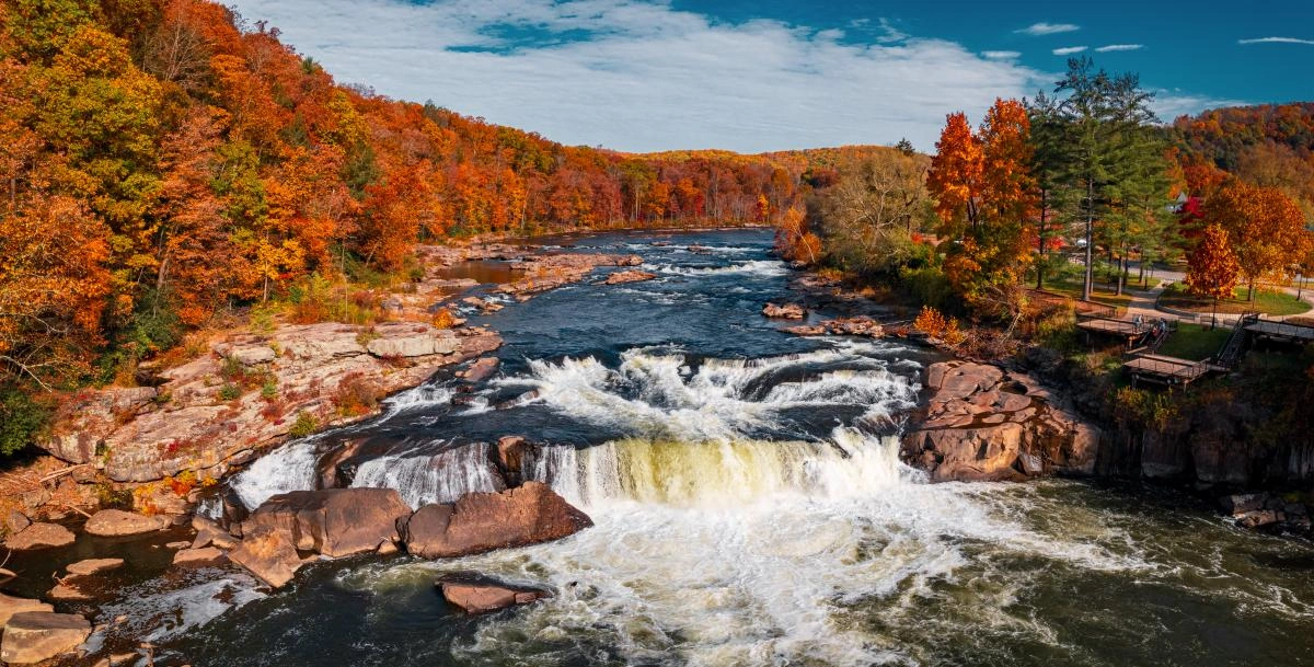 Scenic waterfall in autumn forest with vibrant fall foliage and blue sky.