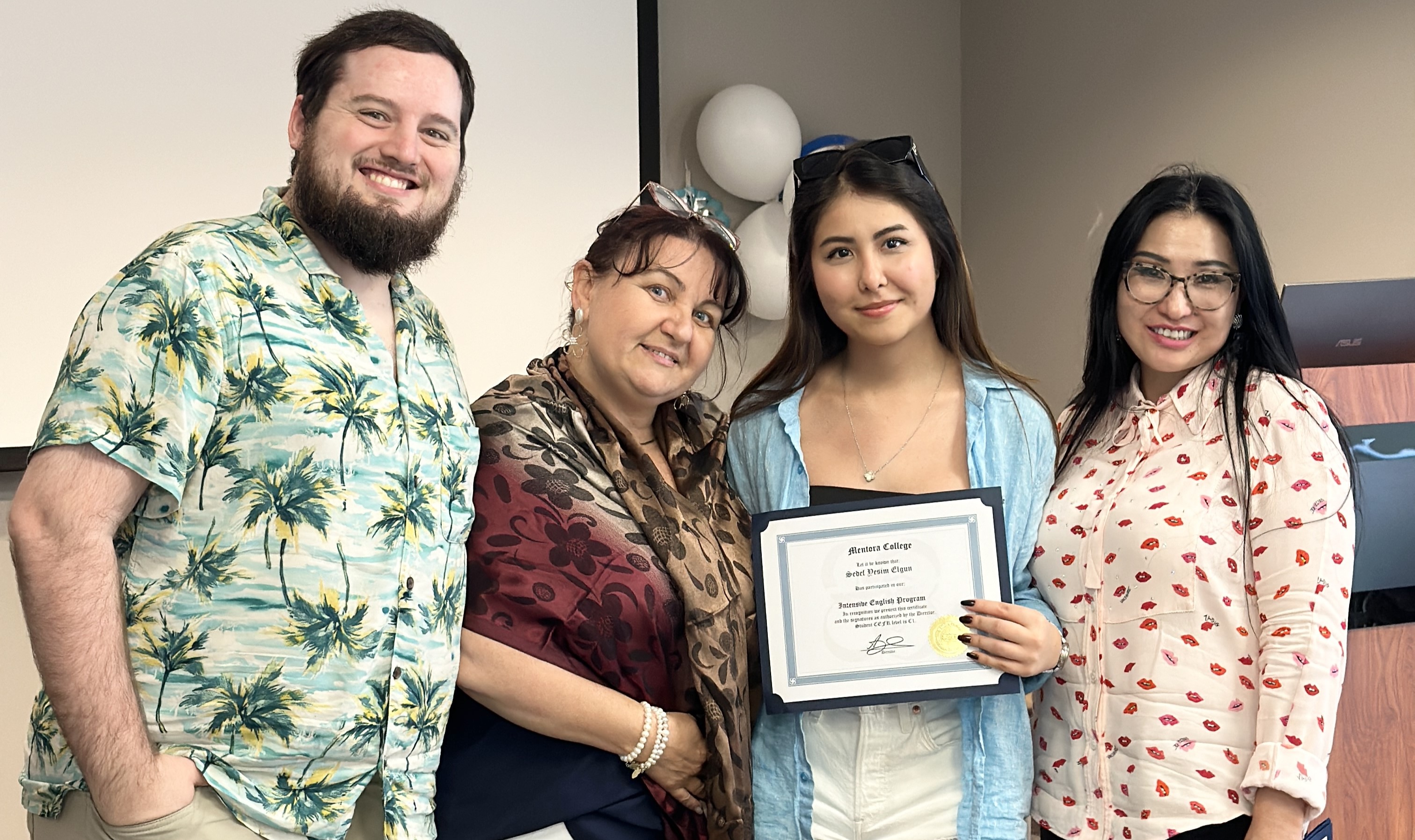 Four people posing for a photo, with one person holding a certificate, smiling together indoors.