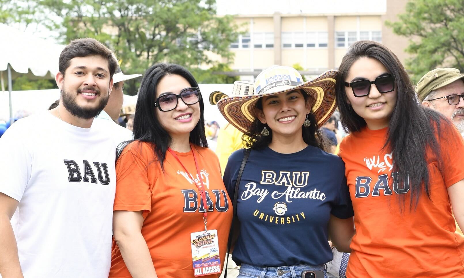 A group of four people wearing BAU t-shirts, smiling together outdoors during a university event.