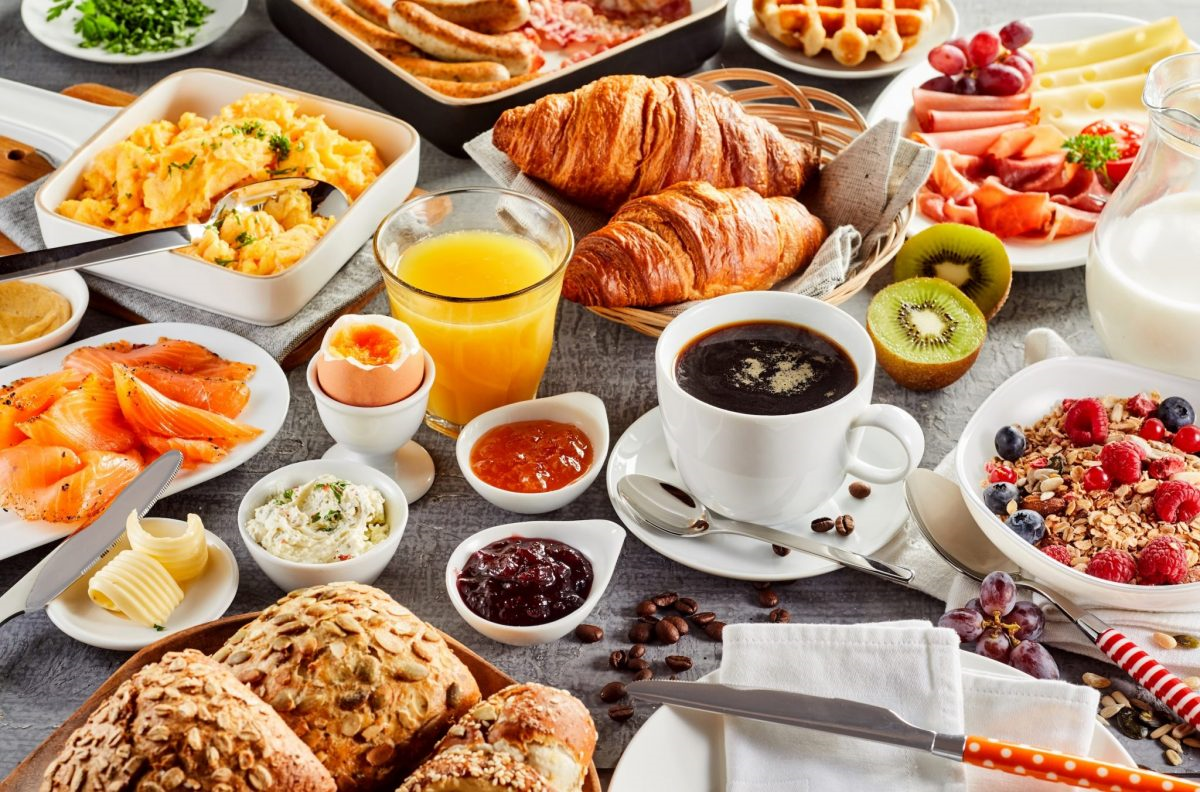 A table filled with a variety of breakfast foods, including coffee, croissants, fruit, bread, jam, and eggs.