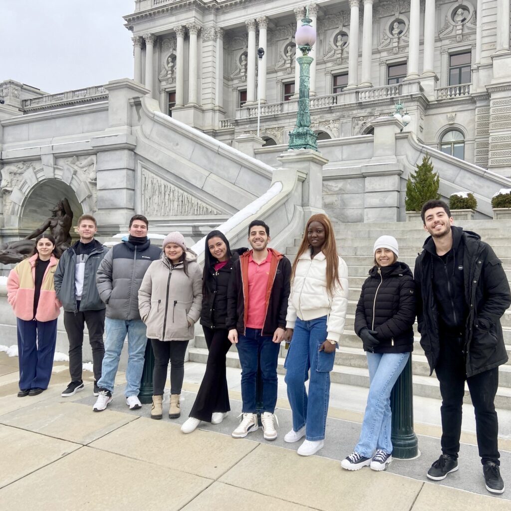 20240119_134738749_iOS Group of people posing in front of a historic building with ornate architecture on a cloudy day.