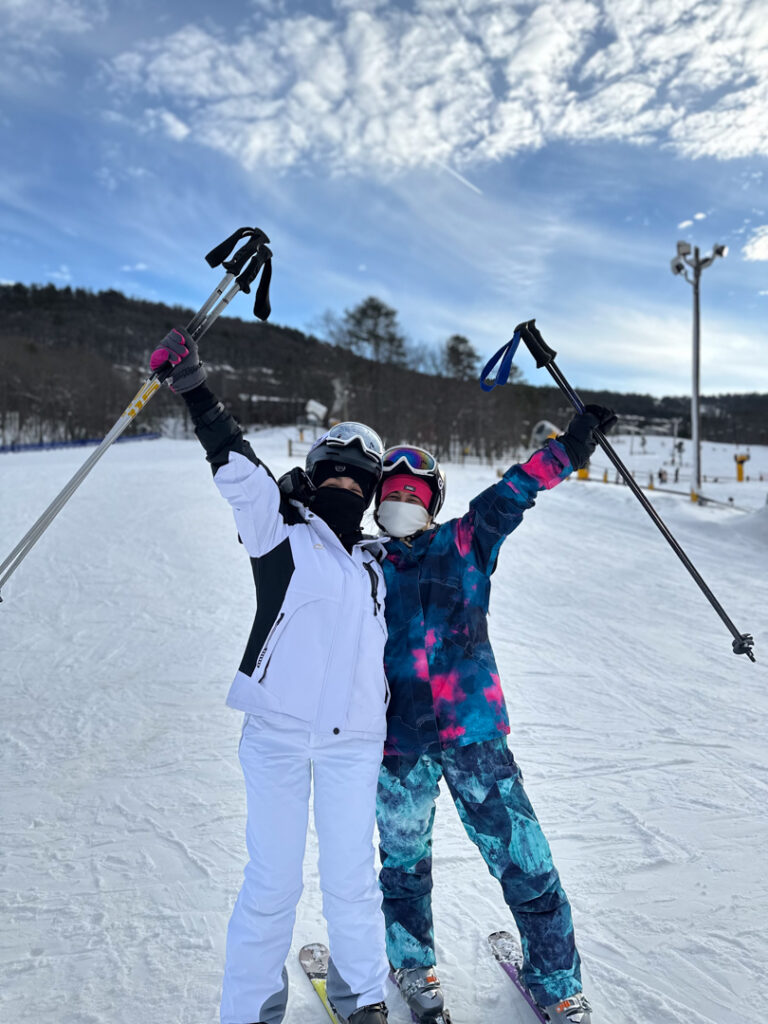 20240122_211655144_iOS Two skiers cheerfully pose on a snowy slope with clear blue skies in the background.