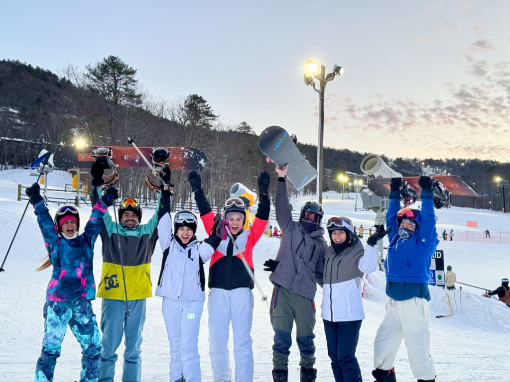 20240122_223445709_iOS Group of friends celebrating on a ski slope at sunset, holding snowboards and ski poles aloft.