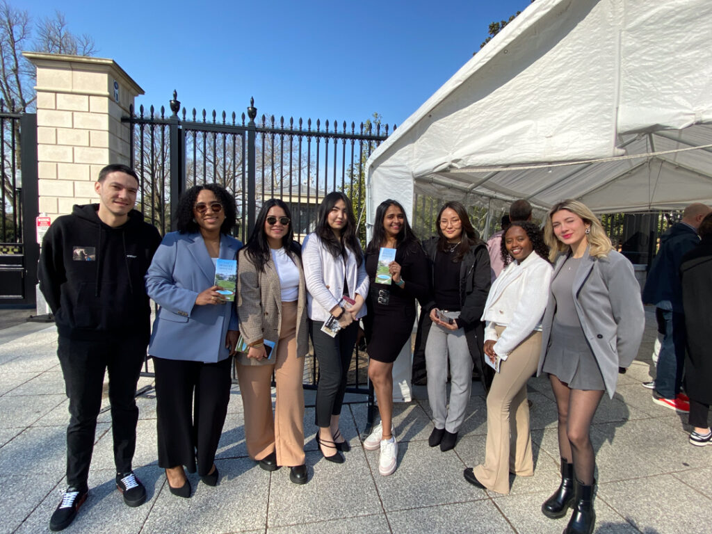 20240227_150304258_iOS Group of diverse professionals smiling outdoors by a tent on a sunny day, holding brochures.