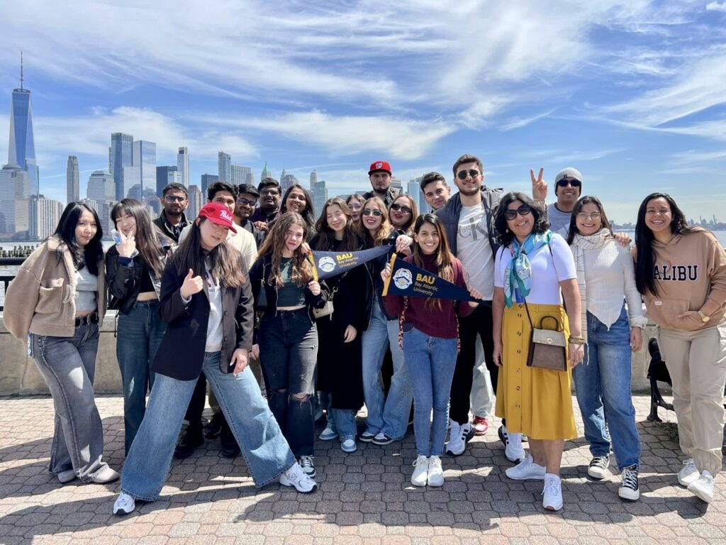 20240606_134959530_iOS Group of people posing with a flag in front of a city skyline under blue sky.