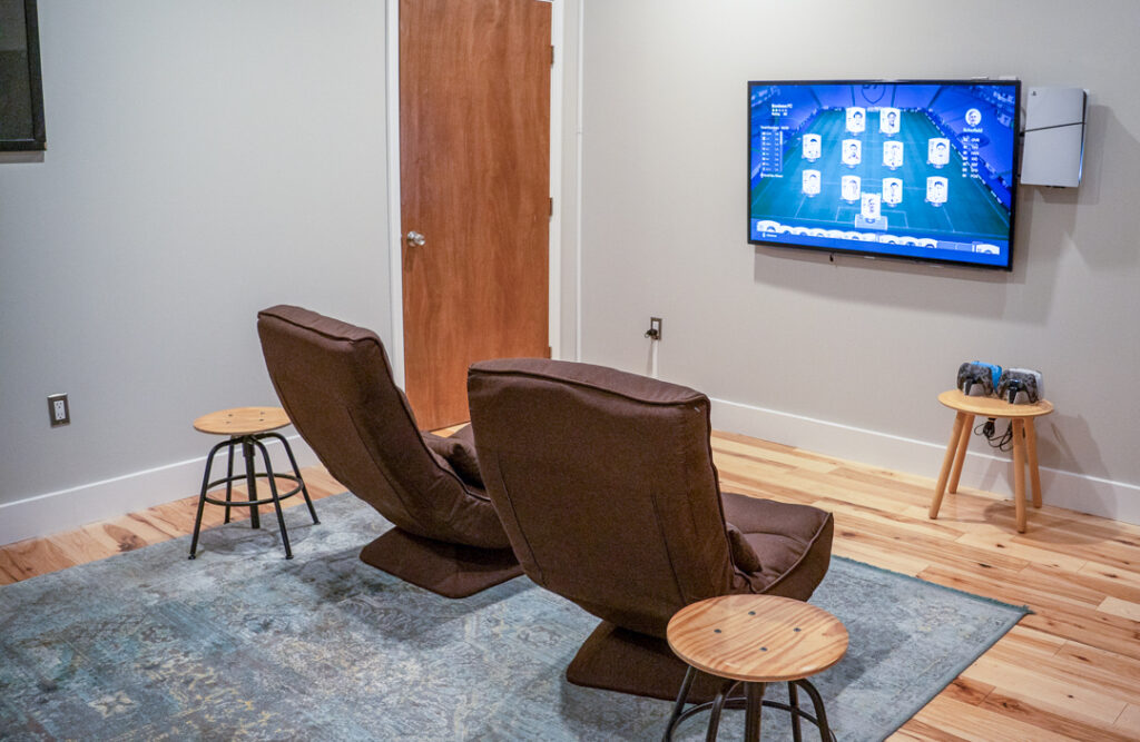 GAME ROOM Gaming room with two chairs, wall-mounted TV displaying a video game, and controllers on a small table.