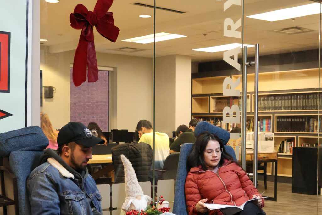 LIBRARY People reading in a cozy library lounge with holiday decor nearby, shelves full of books in the background.