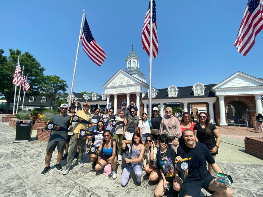 IMG_1444 Group of people posing in front of Six Flags entrance with American flags and a clear blue sky.