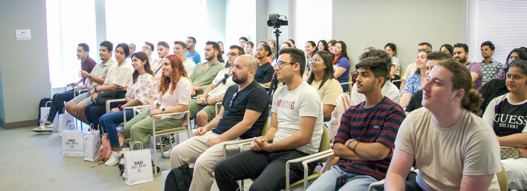 A large group of young adults sit in rows of chairs and look forward.