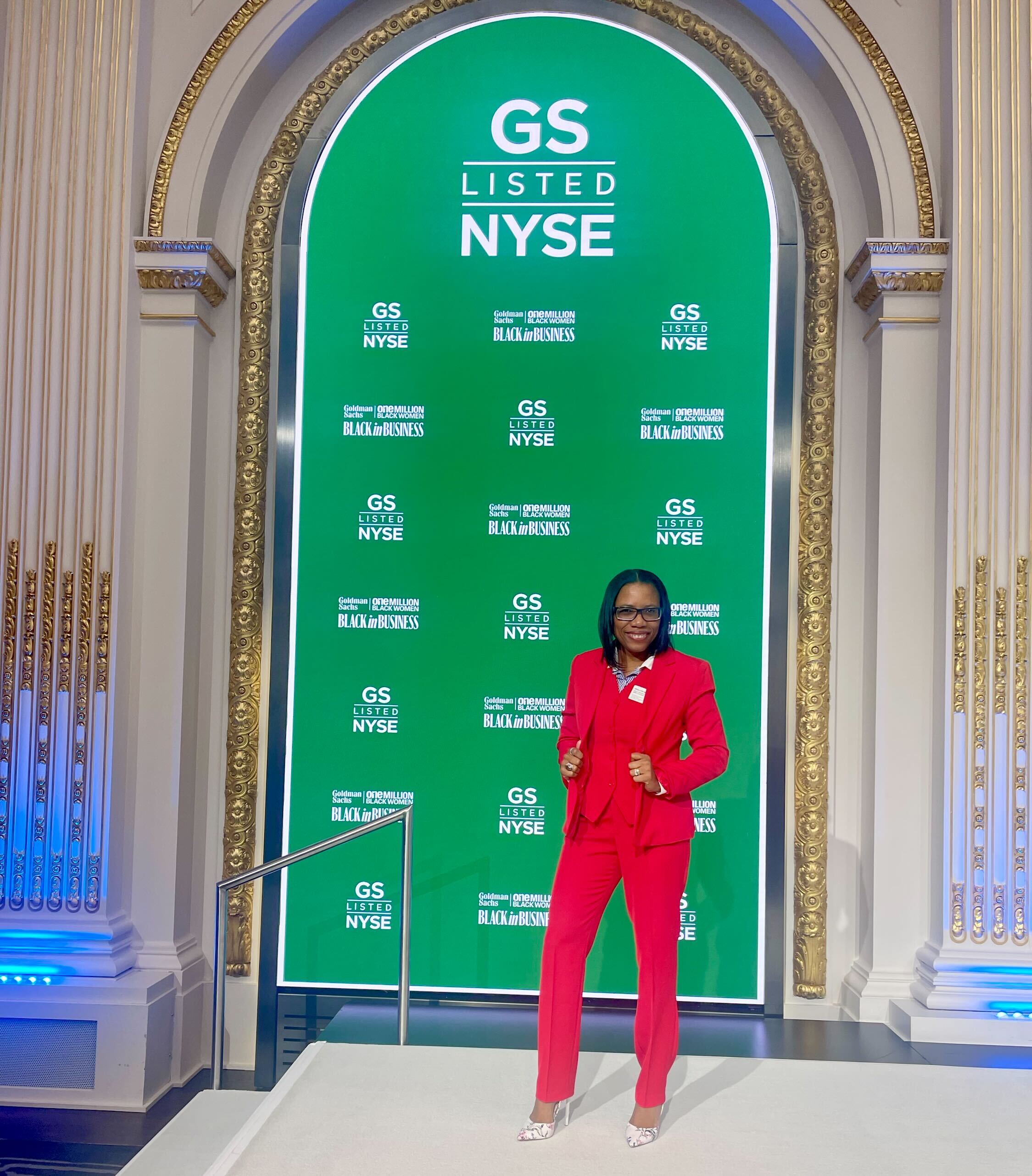 A professionally-dressed woman standing in front of a large archway and digital display board.